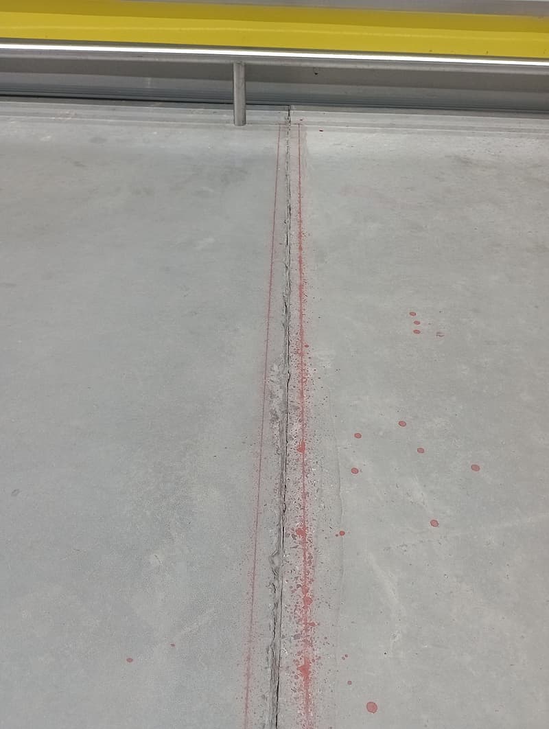 Junta de piso com bordas quebradas marcada em vermelho no corredor de congelados de um atacadista, ao lado dos expositores