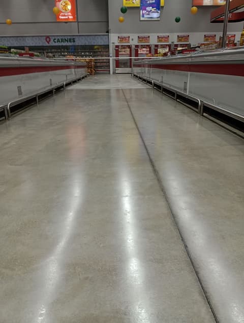 Corredor de congelados com o concreto polido refletindo as luminárias, entre as ilhas refrigeradas