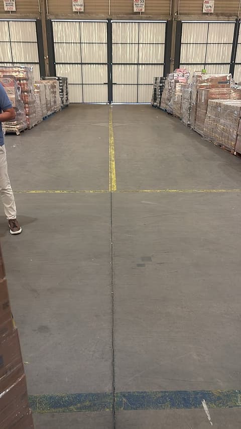Rua de centro de distribuição com piso de concreto e junta longitudinal com bordas desgastadas, mercadoria nos dois lados