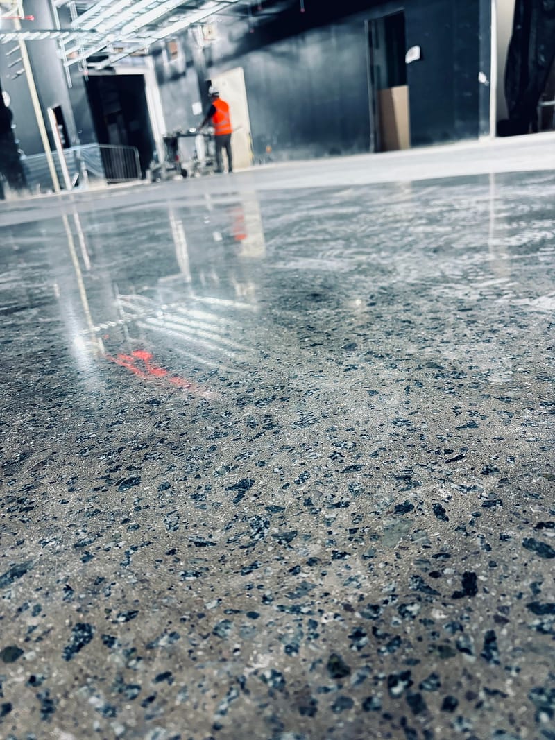 Concreto lapidado com agregado exposto em tons de azul e cinza, refletindo a estrutura metálica do galpão