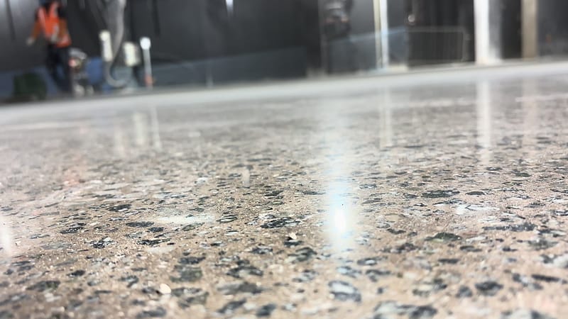 Detalhe rente ao chão do concreto lapidado com agregado exposto e reflexo das luminárias