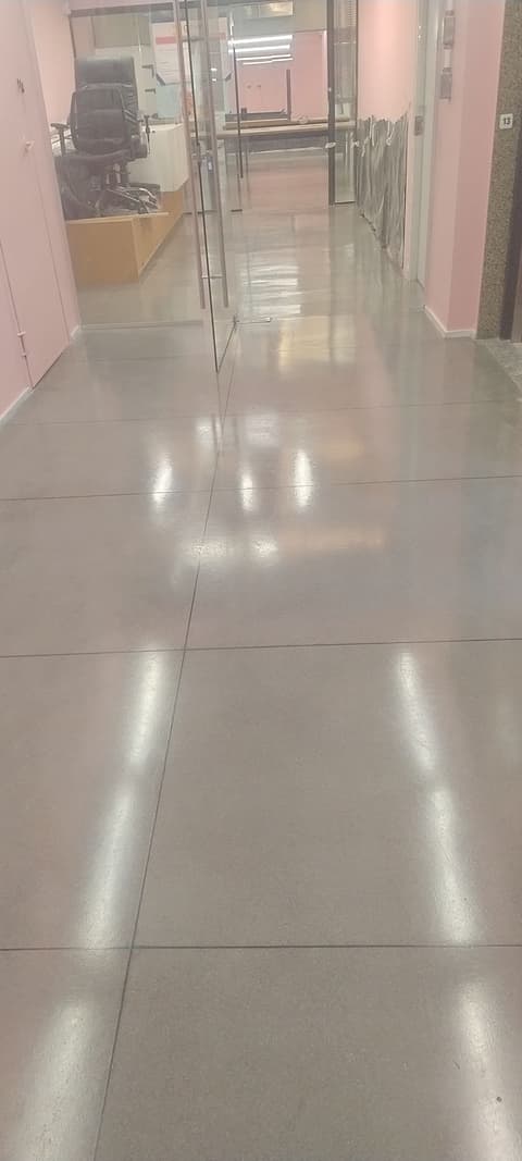 Corredor de escritório com piso de granilite brilhante refletindo as luminárias