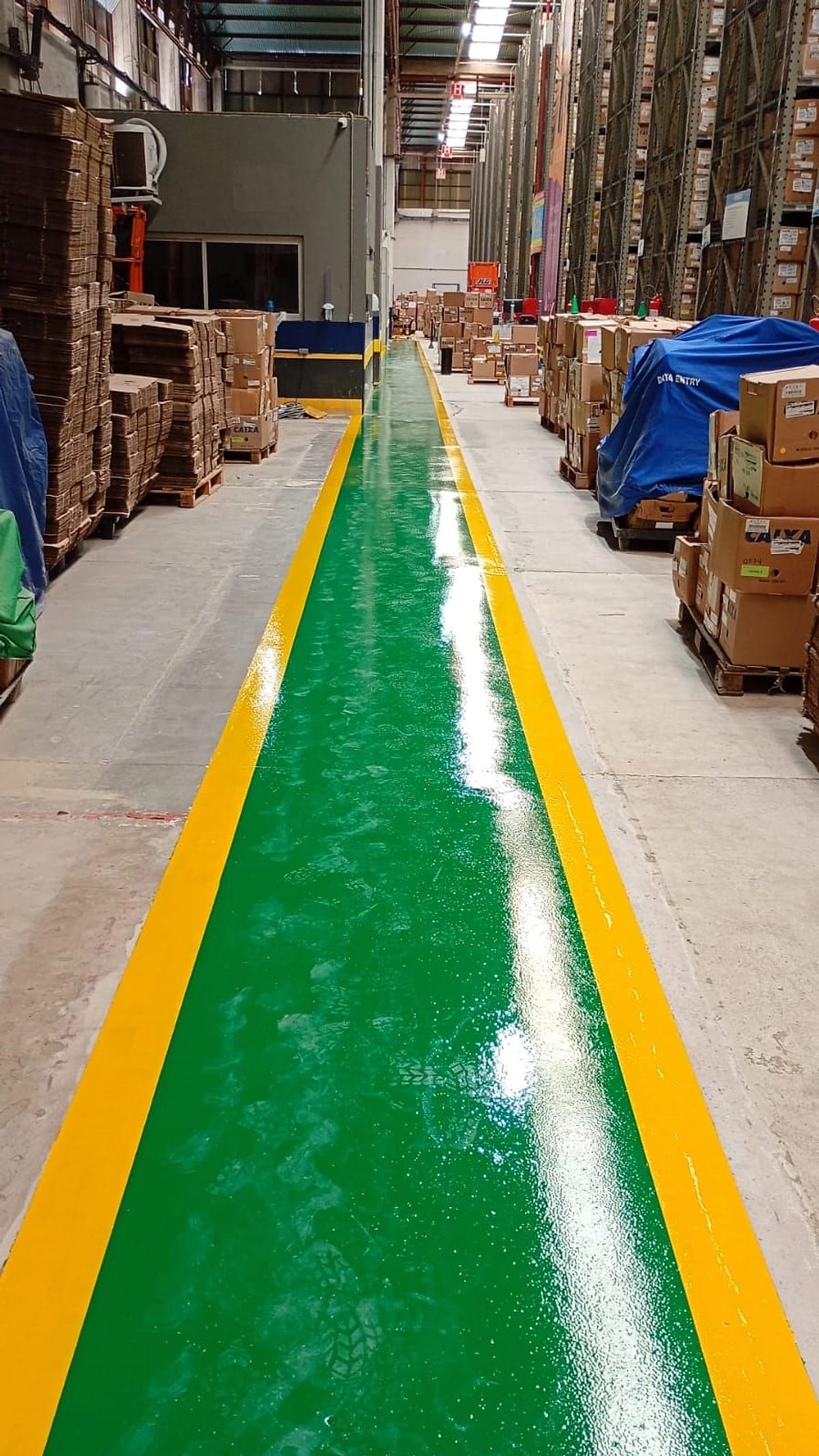 Faixa de pedestres em pintura epóxi verde com bordas amarelas, entre pilhas de caixas, em armazém da Iron Mountain em Barueri