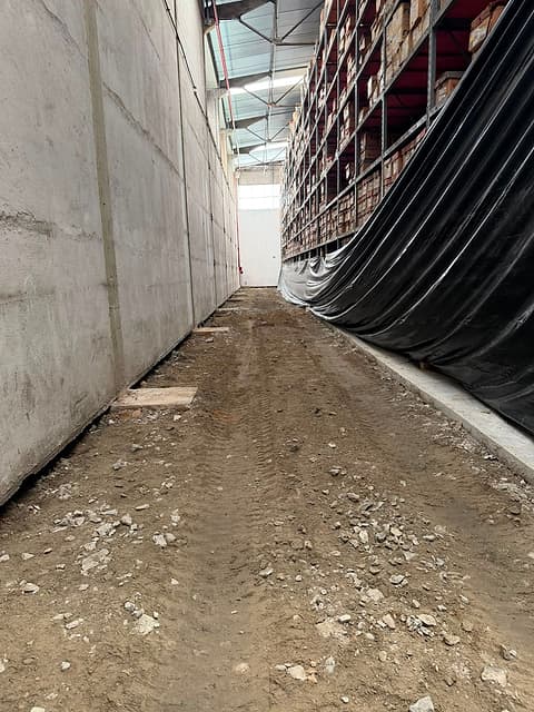 Corredor estreito entre a parede de concreto e as estruturas cobertas, com a base do piso exposta após a demolição