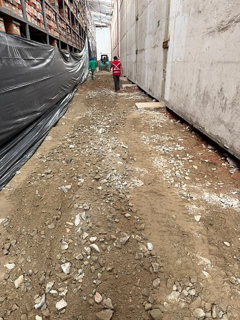 Vista ao longo da faixa demolida, com entulho e sub-base entre a parede e as estruturas de armazenagem