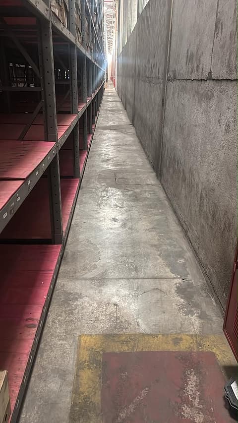 Corredor longo com o piso reconstruído entre as estruturas de armazenagem e a parede de concreto