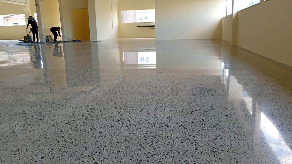 Piso de concreto lapidado com agregado exposto na Cliptech, em São Bernardo do Campo, refletindo paredes e janelas, com dois operadores ao fundo
