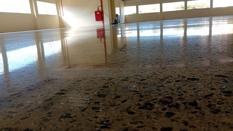 Vista rente ao piso de concreto lapidado com agregado exposto na Cliptech, em São Bernardo do Campo, refletindo a faixa de janelas