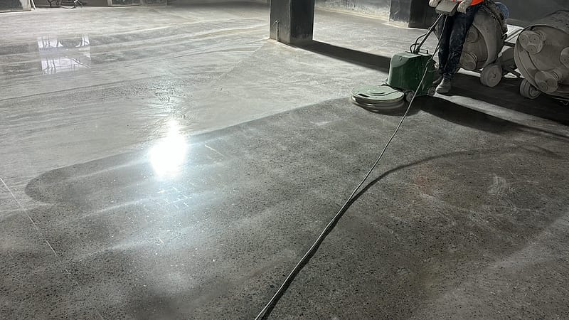 Politriz sobre a linha que separa o concreto bruto do trecho já lapidado, em galpão industrial