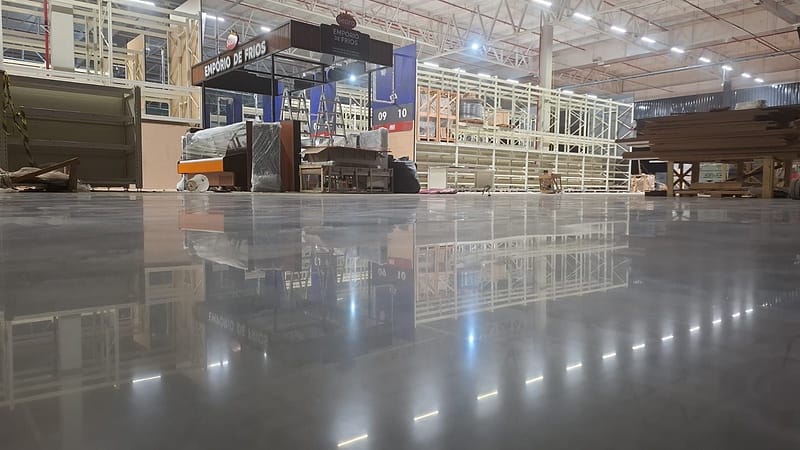 Piso de concreto lapidado com brilho espelhado em loja de atacarejo em montagem, refletindo gôndolas, estande e luminárias