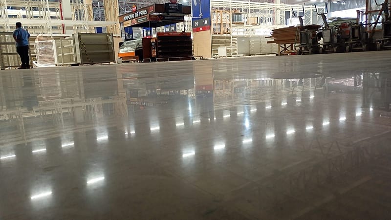 Piso de concreto lapidado em loja de atacarejo, com politrizes estacionadas ao fundo e estrutura da loja refletida no piso