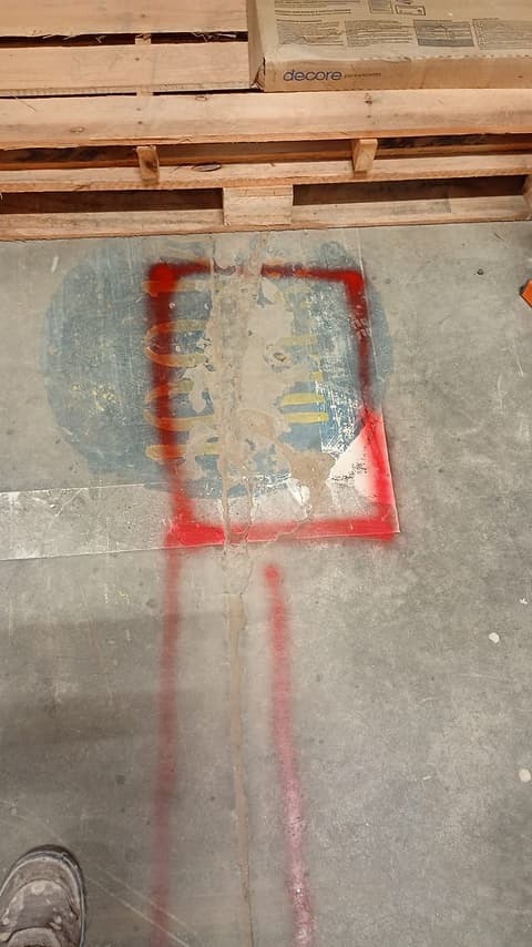 Reparo antigo deteriorado no piso do depósito, marcado com tinta vermelha para a recuperação