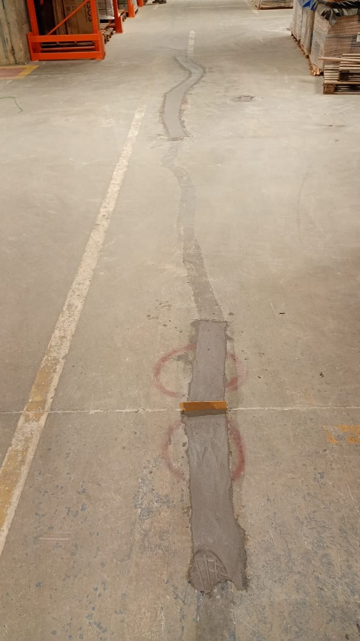 Junta de piso com remendos antigos e marcações vermelhas numa rua de circulação do depósito