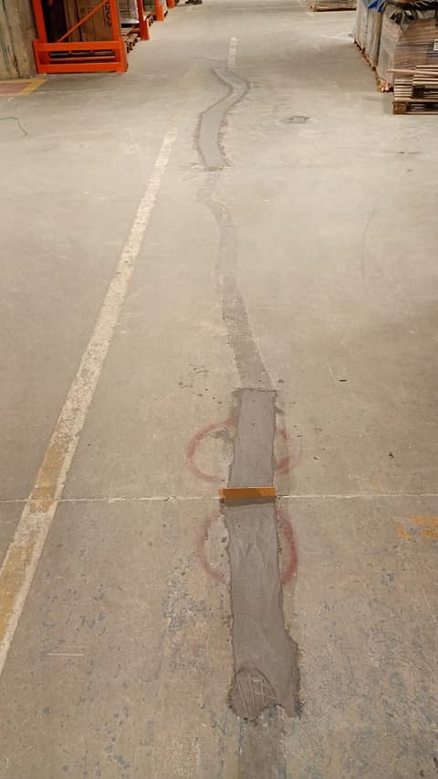 Junta de piso com remendos antigos e marcações vermelhas numa rua de circulação do depósito