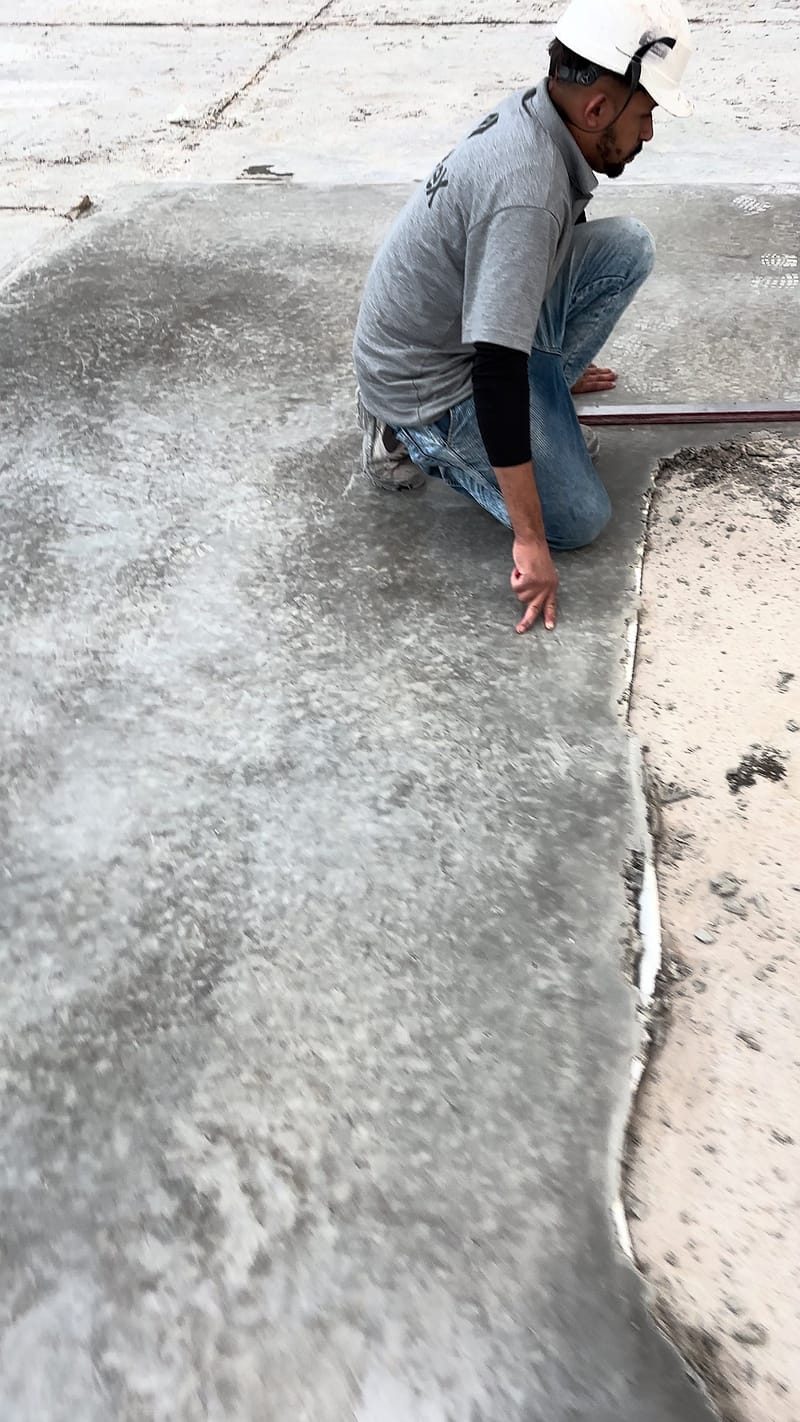 Mão apoiada na linha que separa o concreto bruto do trecho lapidado, em área de teste no piso