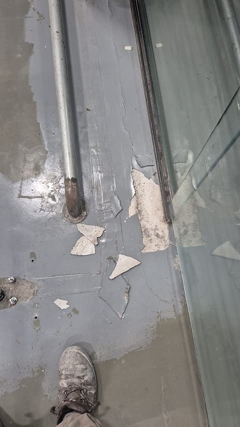 Revestimento antigo descascando em placas junto à porta de vidro da loja