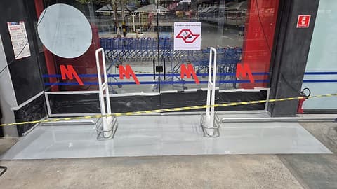 Vista frontal da entrada da loja com o revestimento cinza claro e as cancelas de carrinhos