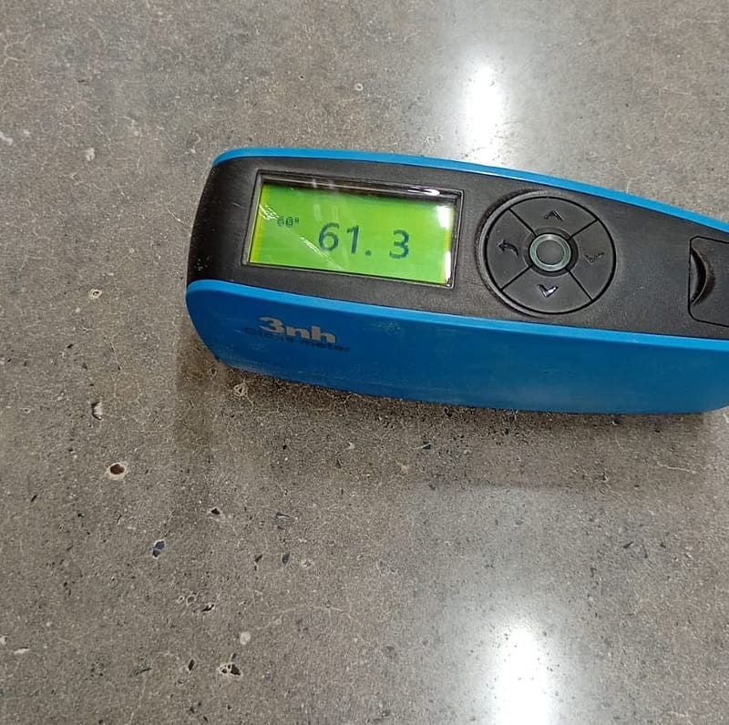 Medidor de brilho apoiado sobre o piso de concreto lapidado do Max Atacadista de Salto, com leitura de 61,3 a 60 graus no visor