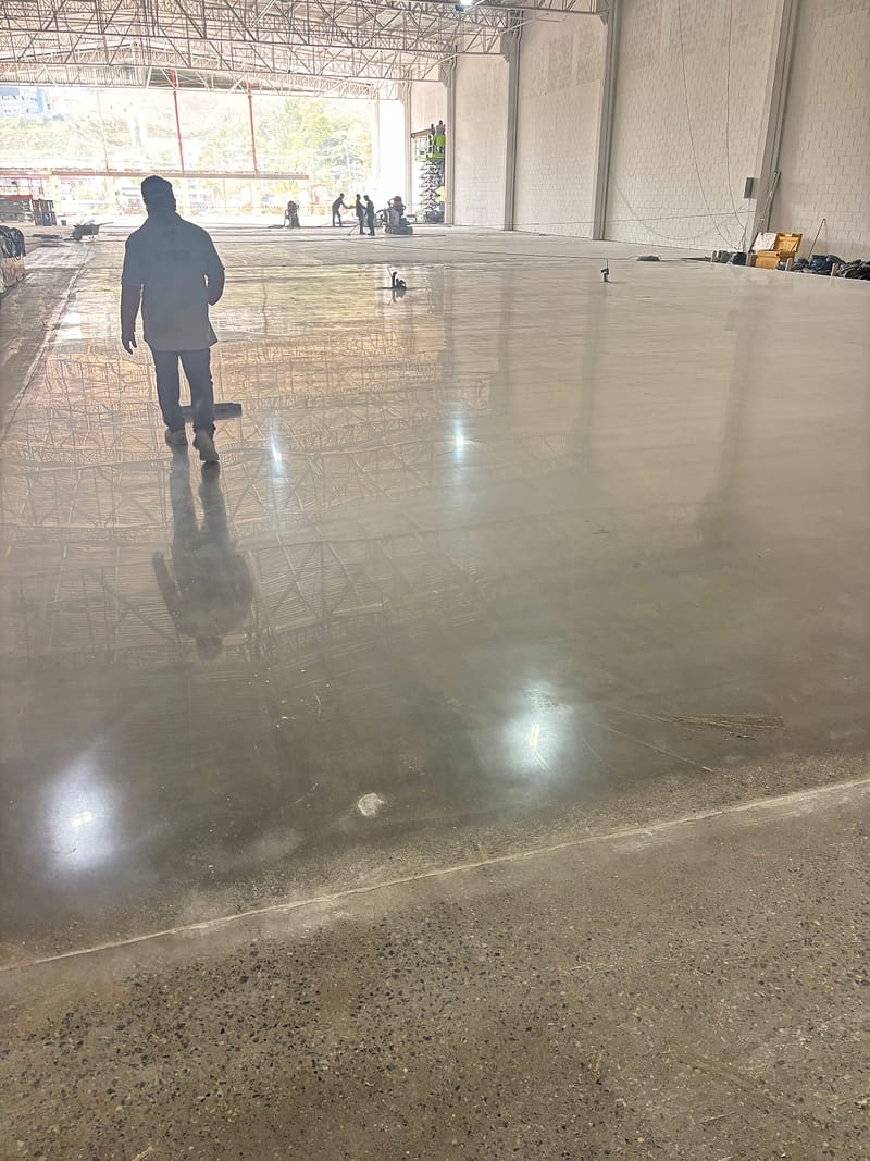 Piso de concreto lapidado visto de cima, com o técnico e a estrutura metálica do galpão refletidos na superfície