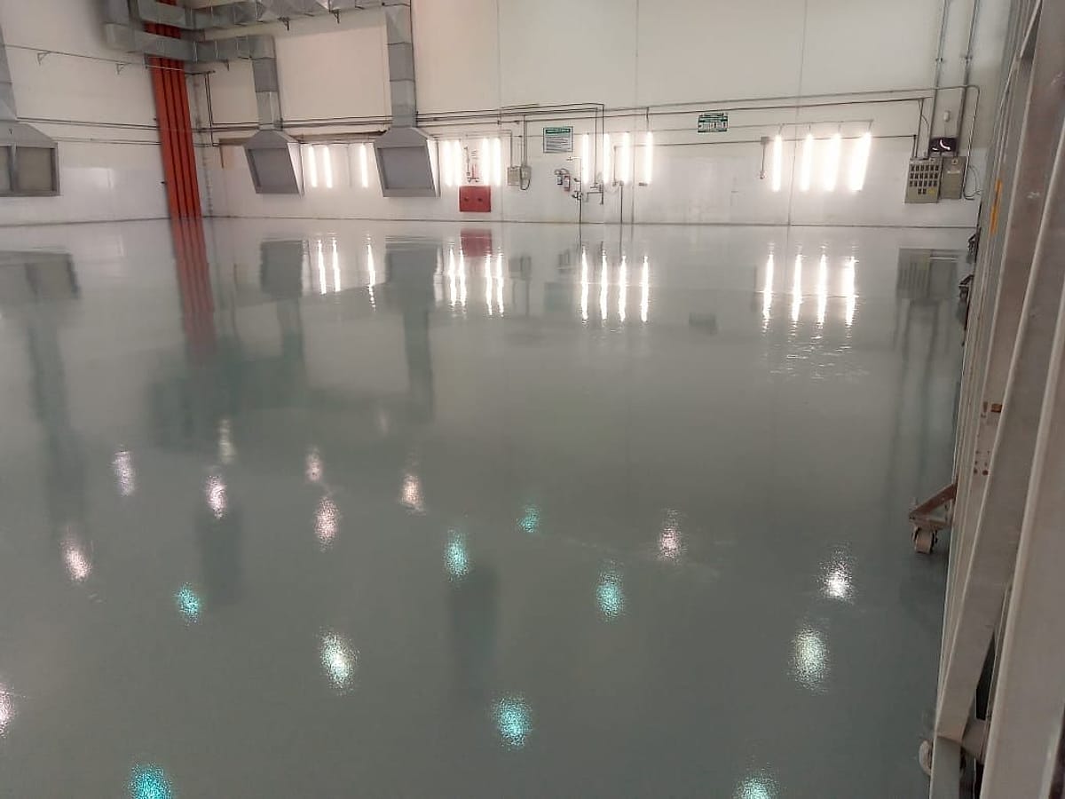 Piso epóxi autonivelante cinza de alto brilho, contínuo e sem juntas, em ampla área de produção