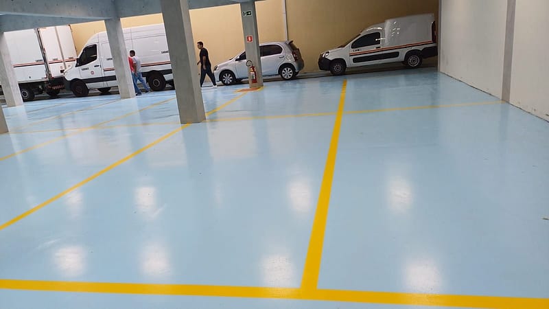 Garagem de veículos utilitários com piso epóxi azul claro e demarcação de vagas em faixas amarelas
