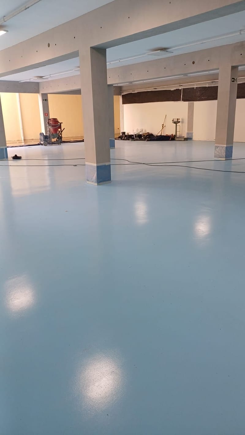 Salão amplo com pilares e piso epóxi azul claro liso e brilhante em fase de acabamento