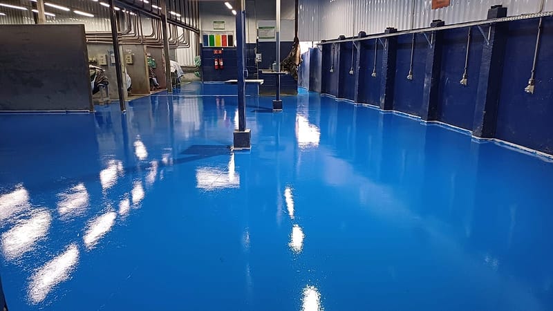 Piso epóxi azul de alto brilho em área industrial com painéis elétricos e tubulações