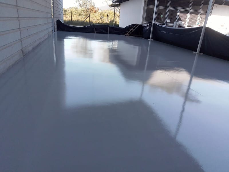 Área coberta externa com revestimento de resina cinza liso refletindo o céu e a estrutura metálica