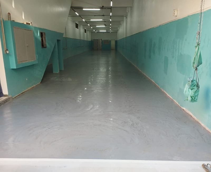 Corredor industrial largo com piso epóxi cinza recém-aplicado e paredes verde-água