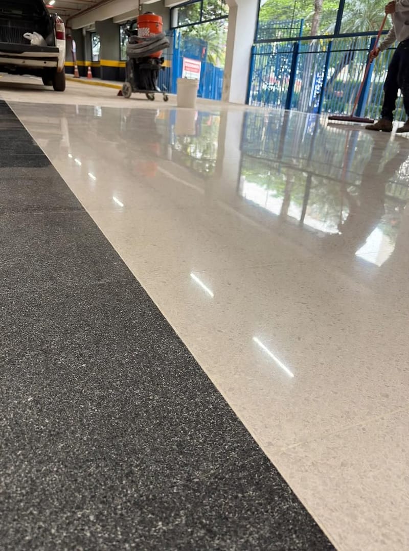 Piso de granilite claro polido em alto brilho, com faixa escura, refletindo a luz em área de grande circulação