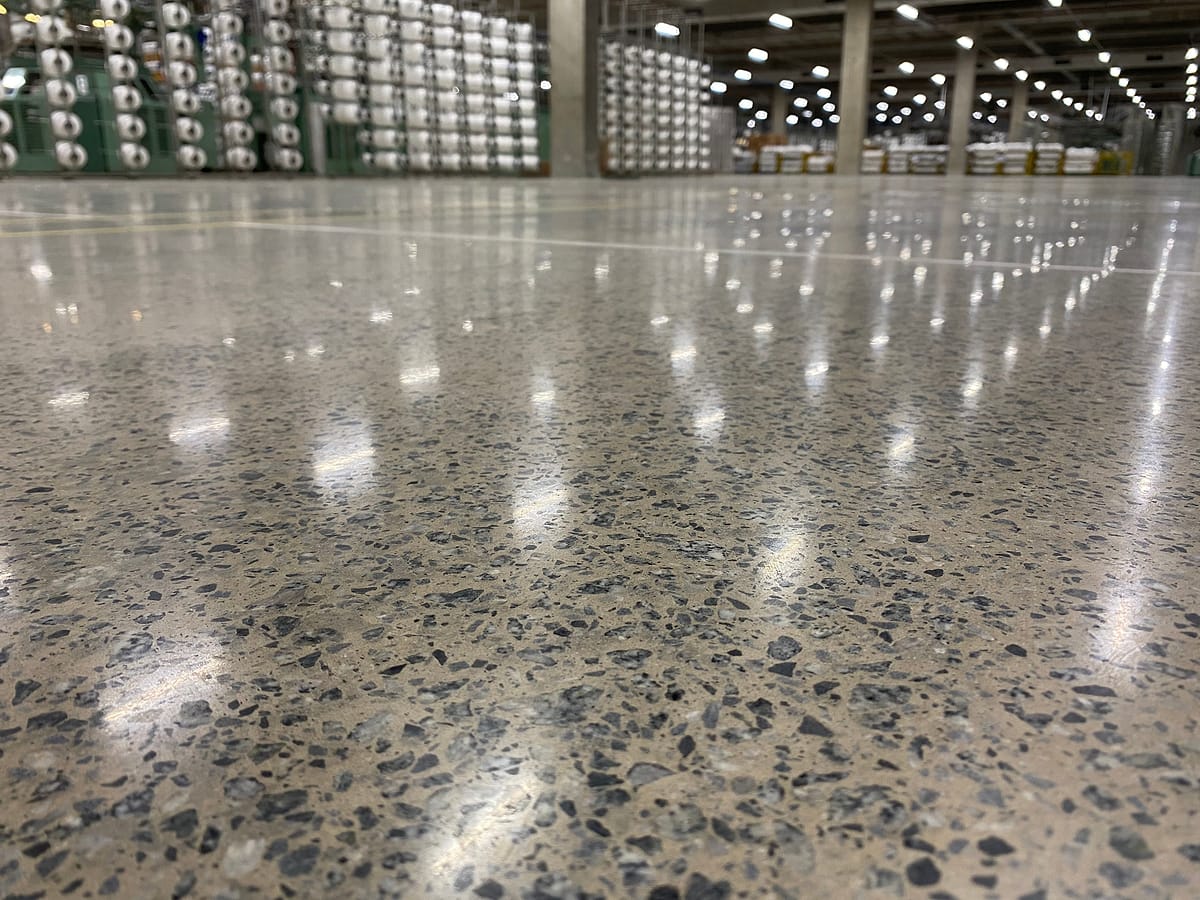 Piso de concreto lapidado em indústria de grande porte com reflexo contínuo das luminárias e bobinas de fio ao fundo
