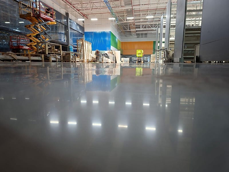 Piso de concreto lapidado no Max Atacadista de Salto, refletindo luminárias, tapumes coloridos e uma plataforma elevatória