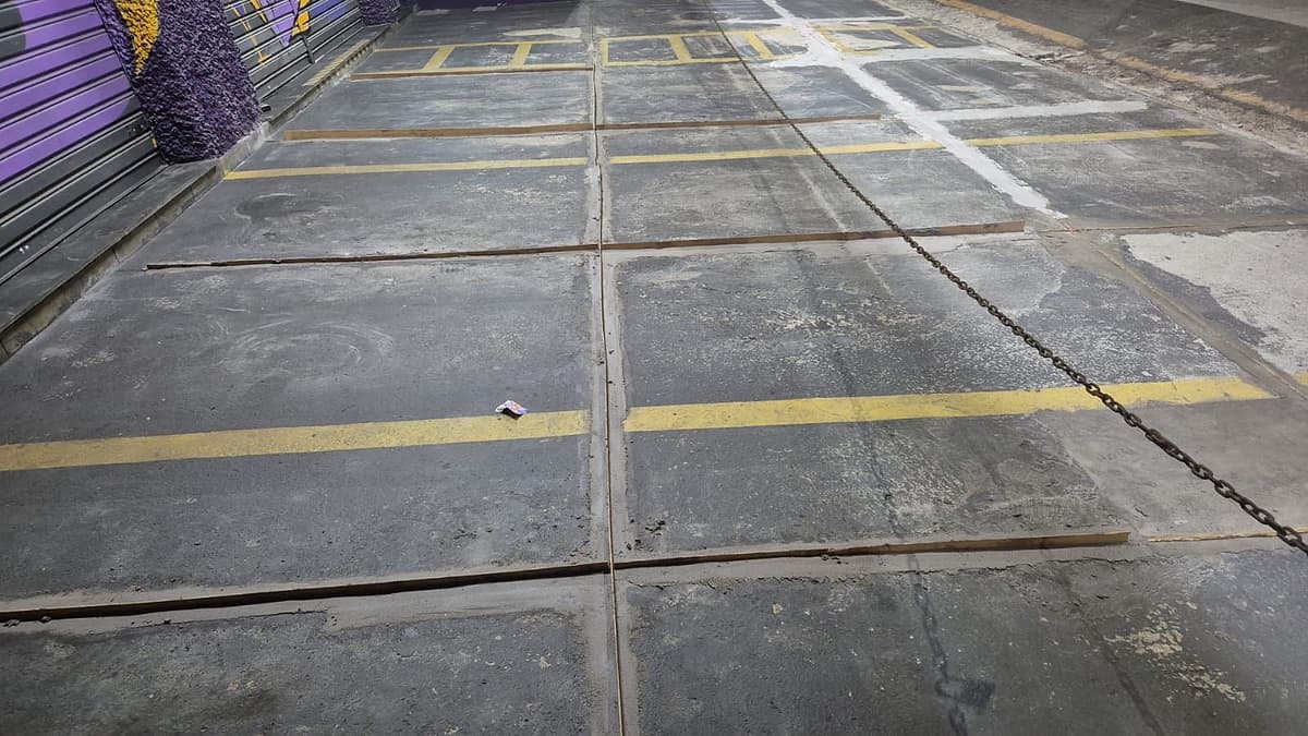 Estacionamento frontal de loja com placas de concreto escurecidas e juntas abertas, isolado por corrente à noite
