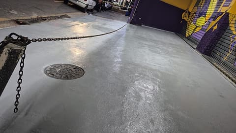 Revestimento cinza na entrada da loja contornando a tampa de inspeção, com corrente de isolamento