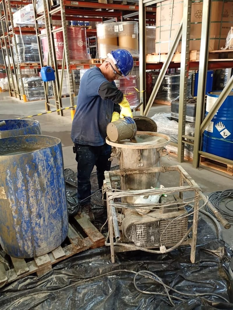 Técnico da Reflex prepara calda de cimento no misturador, ao lado dos tambores e da bomba de injeção, dentro de armazém logístico