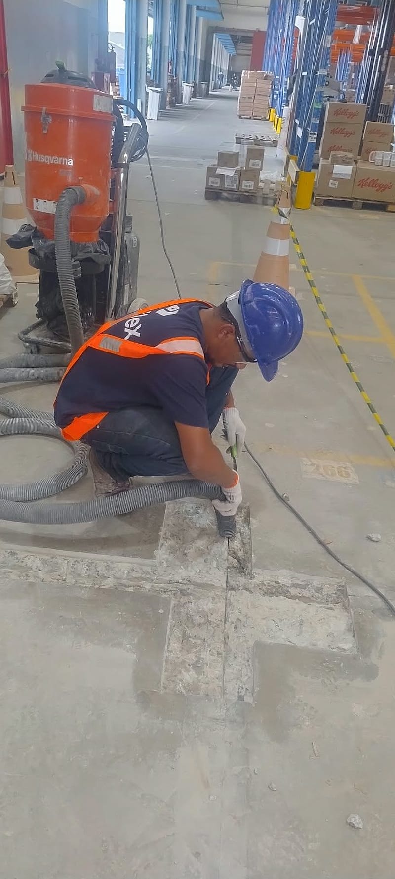 Operador de capacete prepara o cruzamento de juntas aberto no piso, com aspirador industrial ao lado, na Disploki, em Barueri