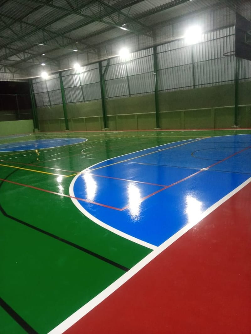 Piso de quadra coberta recém-pintado refletindo os refletores da cobertura metálica