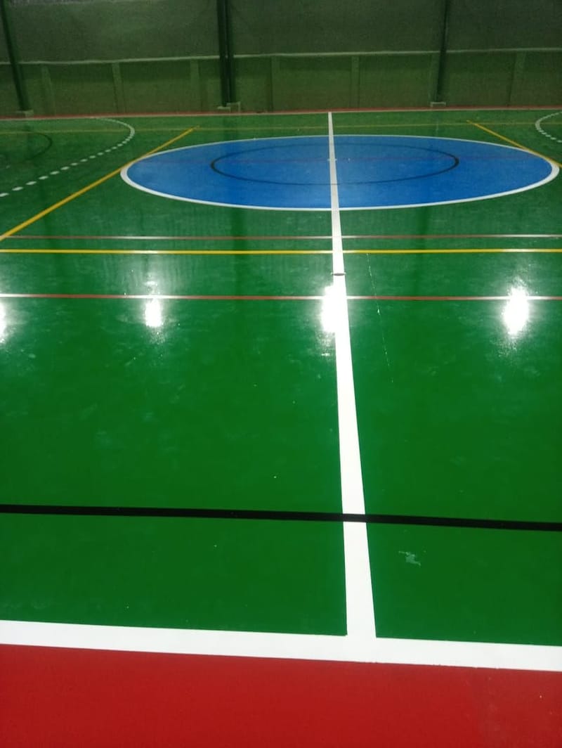 Círculo central azul e linha divisória branca de quadra poliesportiva com linhas amarelas e pretas de outras modalidades