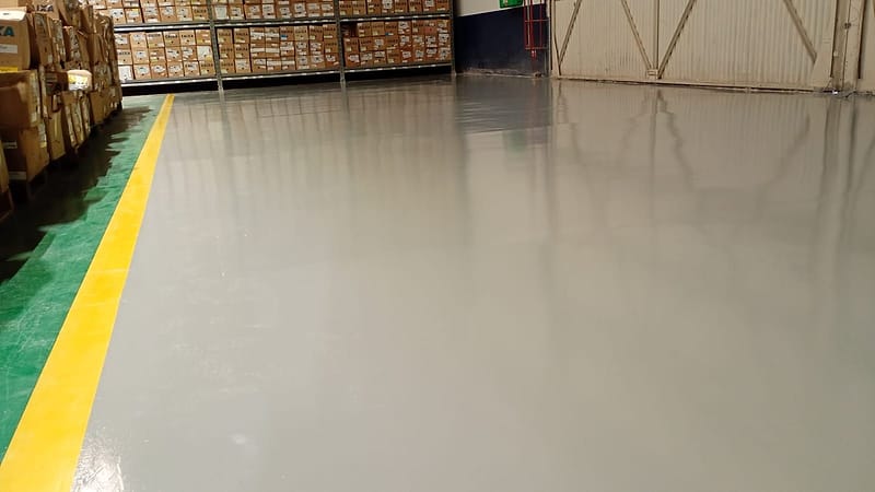 Piso com revestimento de resina cinza brilhante, faixa de demarcação amarela e borda verde em armazém