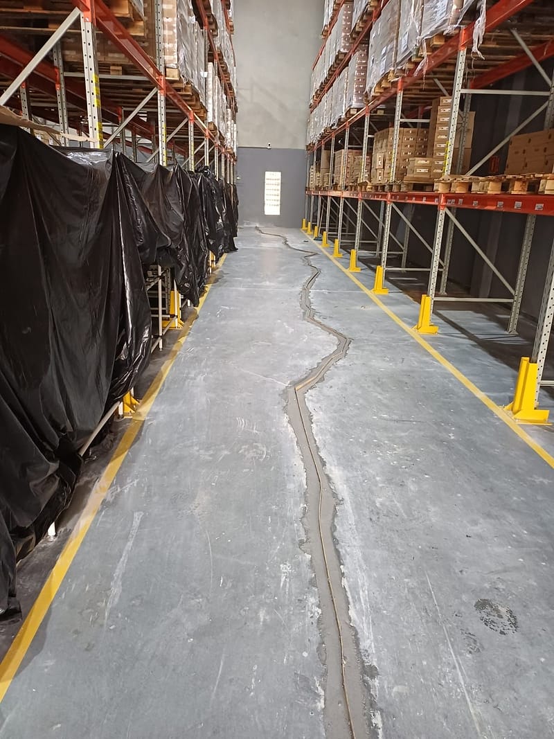 Corredor de centro de distribuição entre estruturas porta-paletes, com uma trinca longa do piso de concreto aberta e preenchida com argamassa polimérica